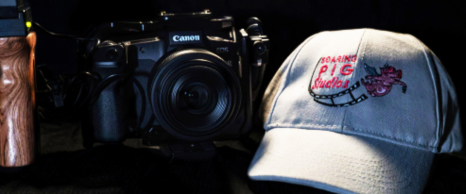 Event and Sports Photography depicted by a professional DSLR camera with a textured grip and a Soaring Pig Studios branded cap on a reflective black surface.