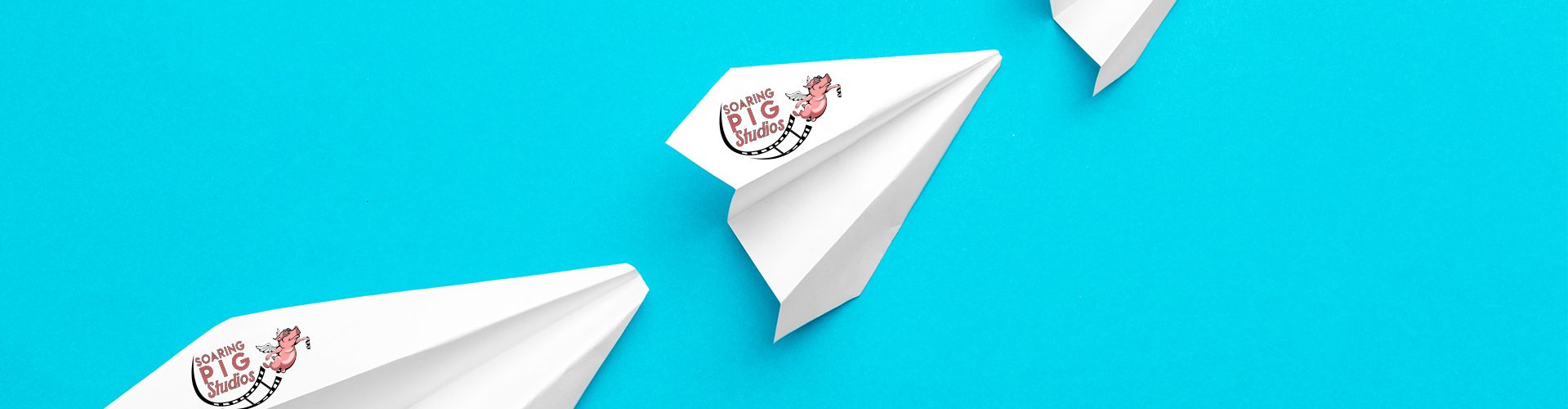 Three white paper planes featuring the Soaring Pig Studios logo, flying in formation against a bright blue background, symbolizing creativity, strategy, and forward-thinking solutions in our work.