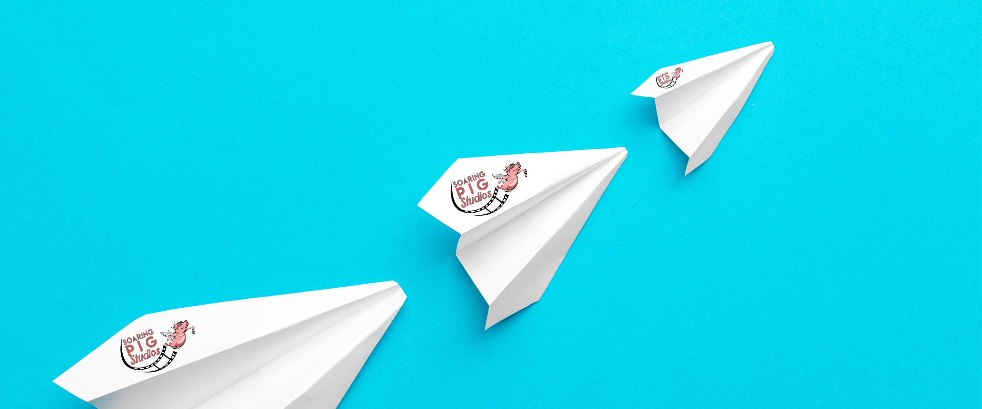 Three white paper planes featuring the Soaring Pig Studios logo, flying in formation against a bright blue background, symbolizing creativity, strategy, and forward-thinking solutions.